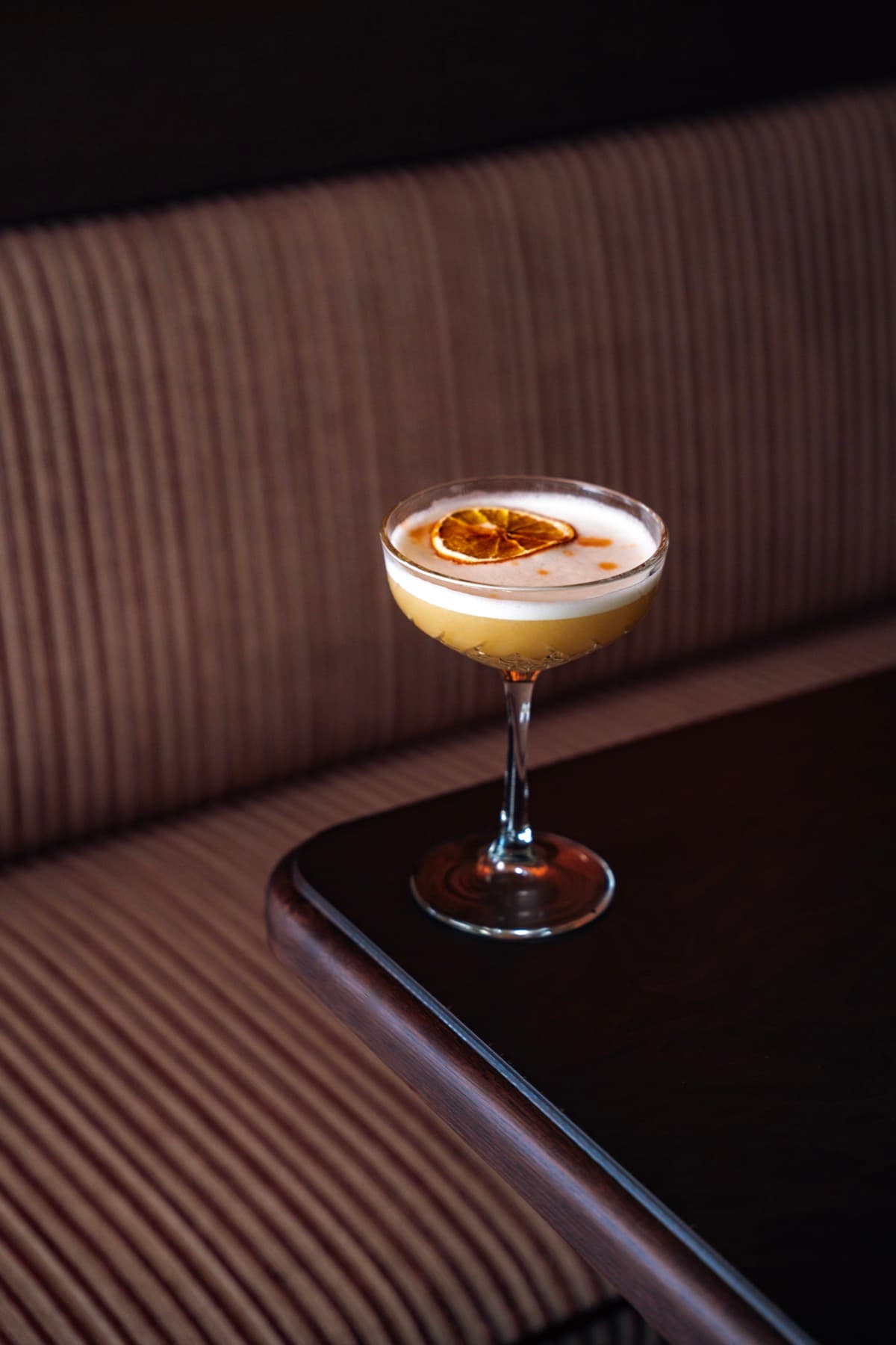 A coupe cocktail garnished with dried orange